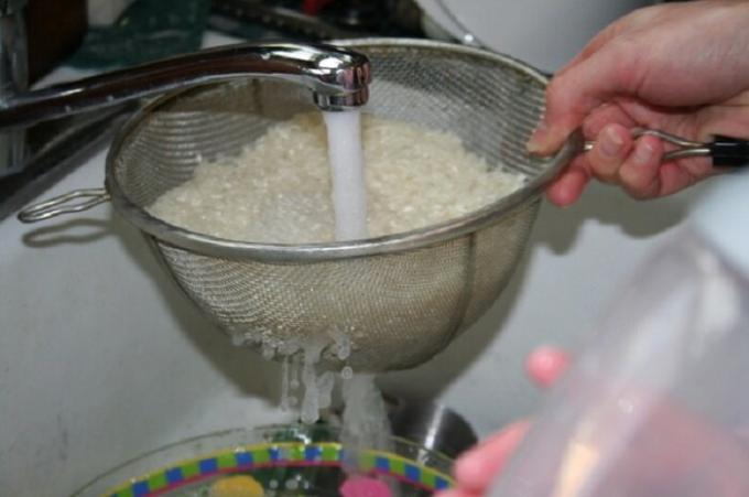 يغسل الأرز في مصفاة مريحة مع المياه الجارية.